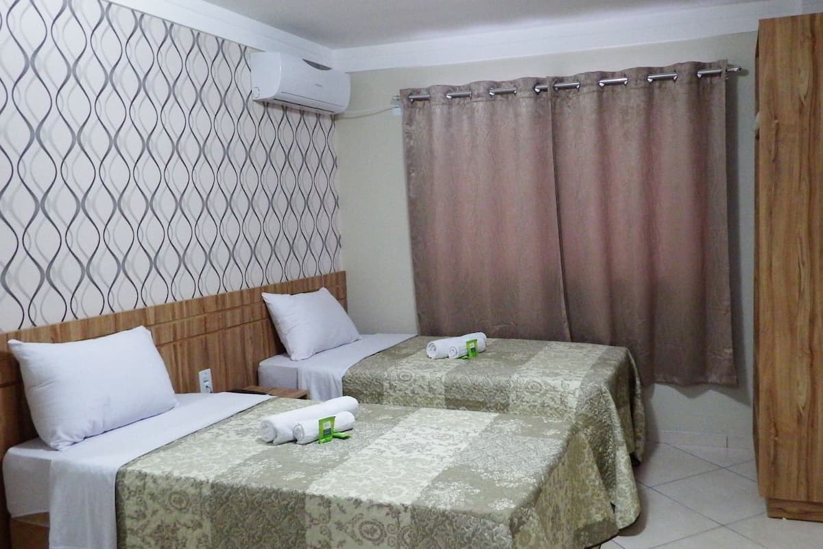 Une chambre d’hôtel avec deux lits, une tête de lit en bois, un papier peint à motifs, un rideau et un téléviseur fixé au mur.