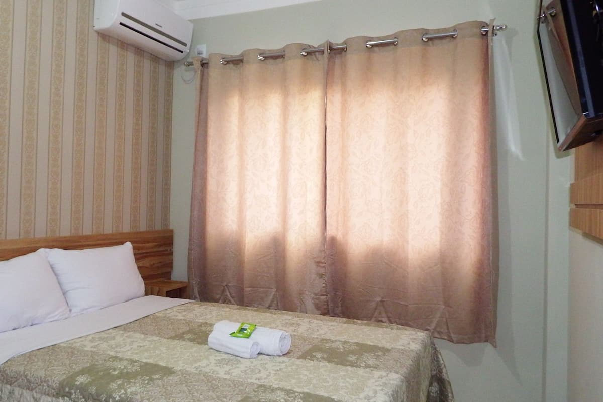 Une chambre d’hôtel avec un lit, un téléviseur fixé au mur et une fenêtre avec des rideaux.