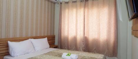 Habitación de hotel con cama, televisor montado en la pared y ventana con cortinas.