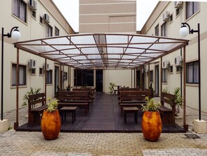 Un espace extérieur abrité, doté de bancs en bois et de grands pots de plantes.