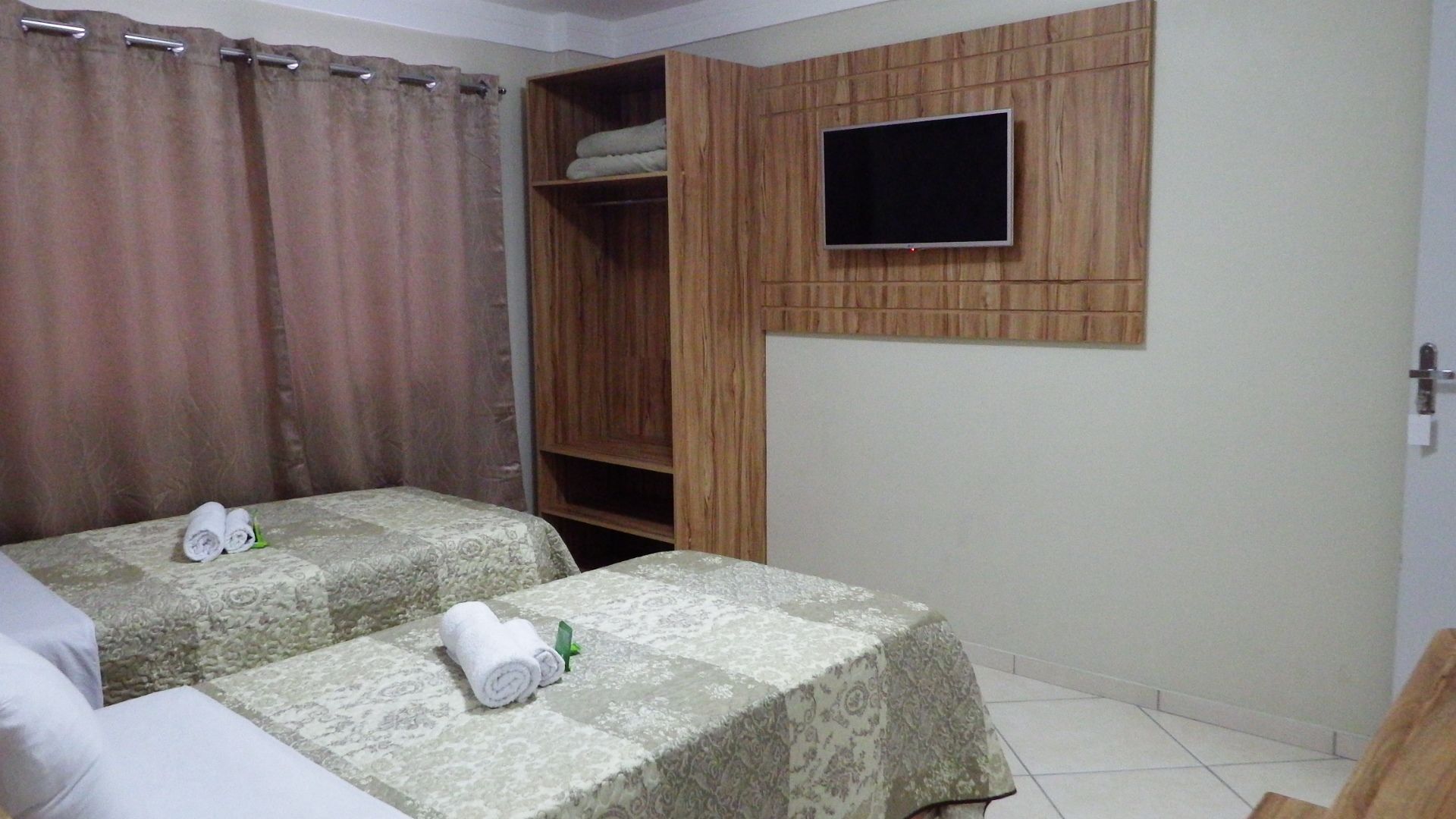 Una habitación con dos camas, un televisor montado en una pared de paneles de madera y un armario.