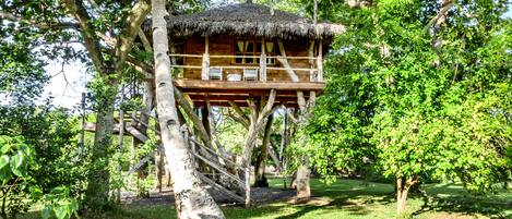 A treehouse with a thatched roof, wooden railings, and a small deck area.