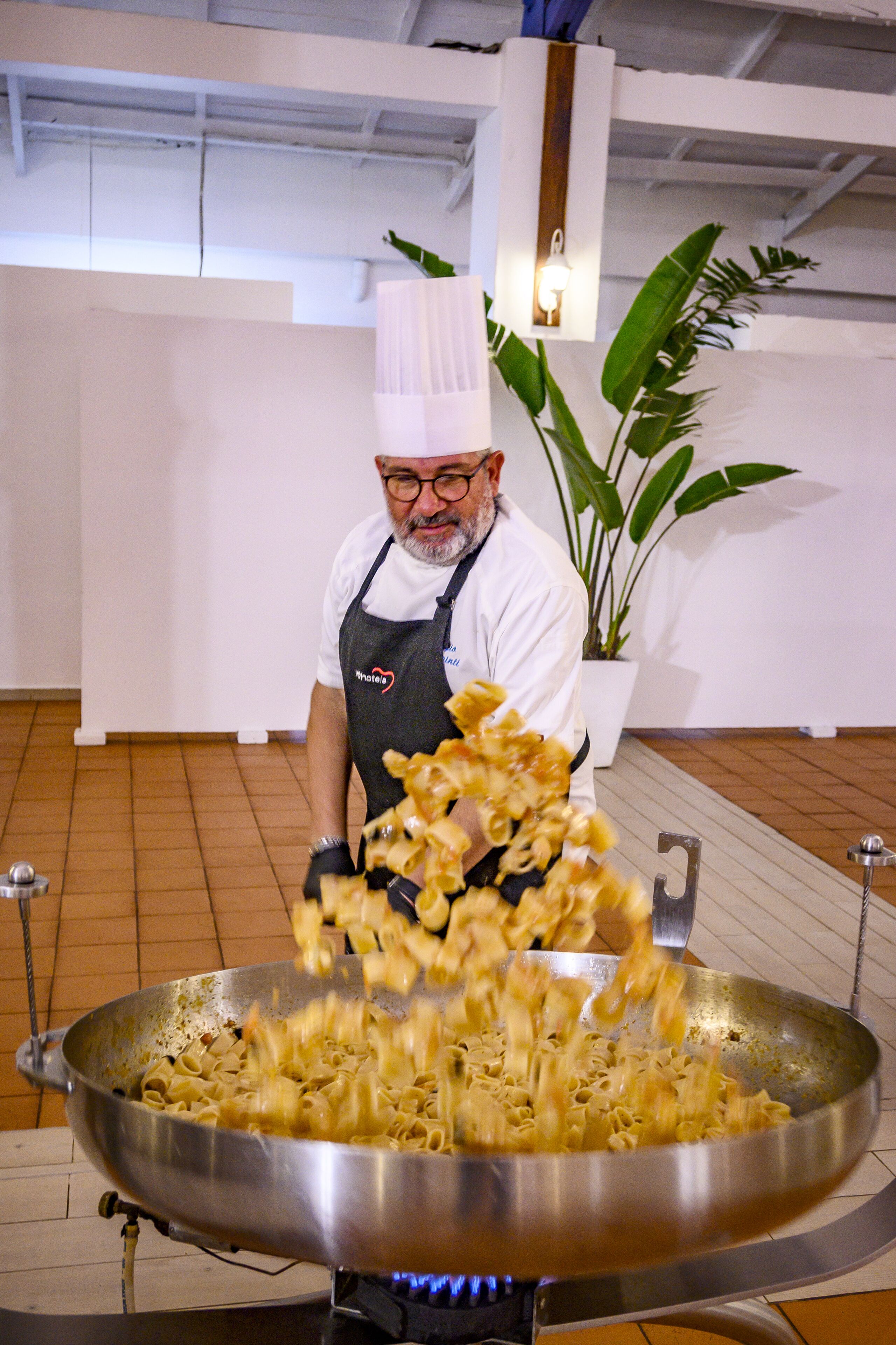 Un xef cuinant pasta en un gran wok sobre un fogó portàtil.