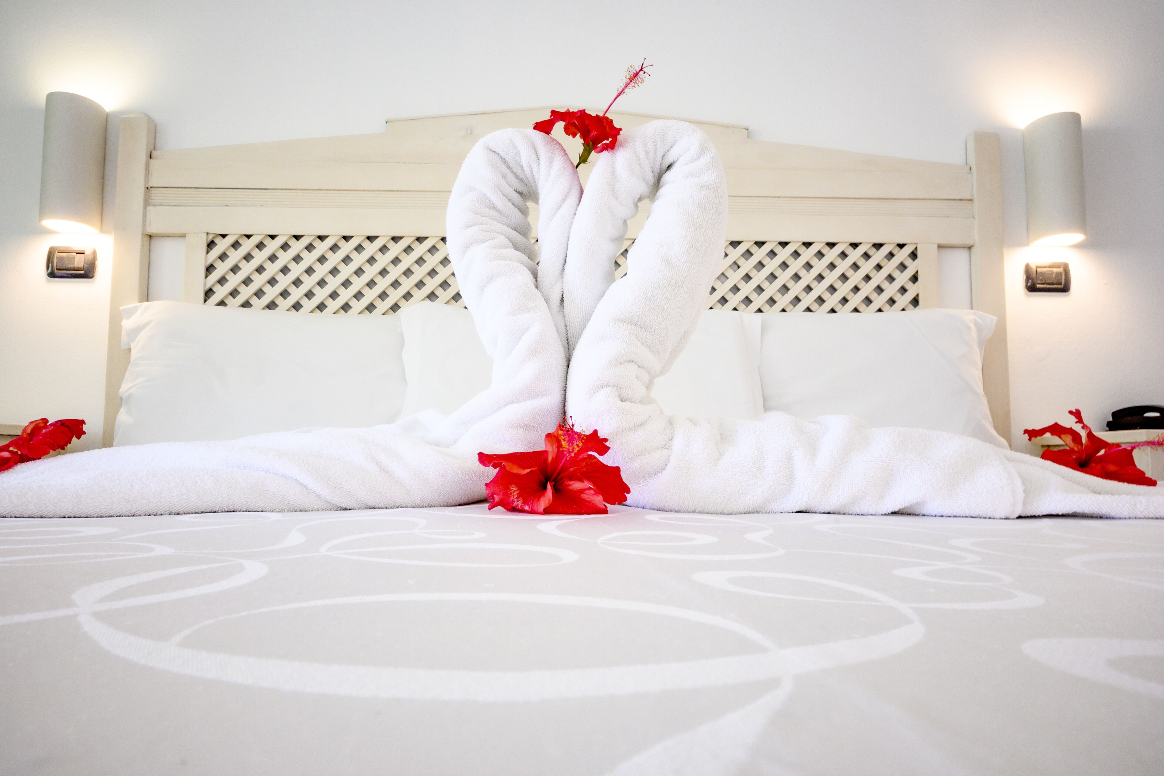 A bed with white linens and red flowers arranged in a heart shape.