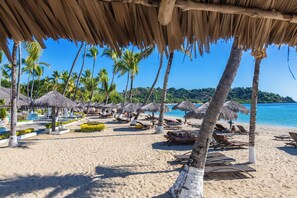 Una playa con sombrillas de paja, palmeras y sillas de descanso.