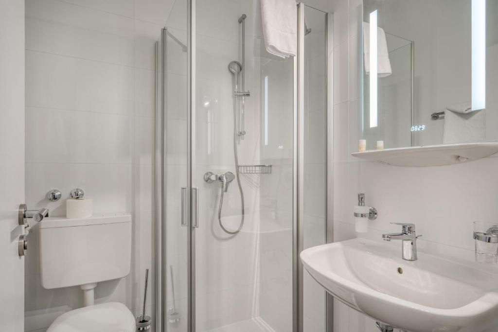 Un baño moderno con ducha envuelta en vidrio, un lavabo blanco y un espejo sobre él.