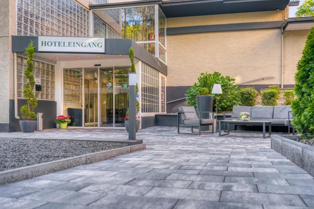 A hotel entrance with a sign reading 'HOTELINGANG,' outdoor seating area with tables and chairs, and a well-maintained garden.