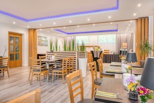 A modern hotel dining area with wooden furniture, a central island, and a view of the garden through large windows.