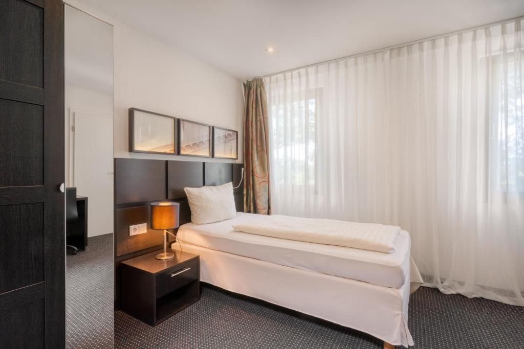 A hotel room with a bed, bedside table, lamp, and curtains.