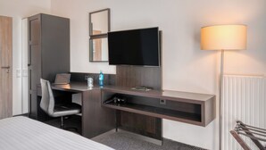 Ein Hotelzimmer mit Bett, Schreibtisch mit Laptop, Fernseher, Spiegel, Lampe und Heizkörper.