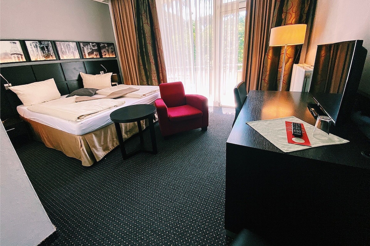 A hotel room with a bed, a desk, a chair, a TV, and a window with curtains.
