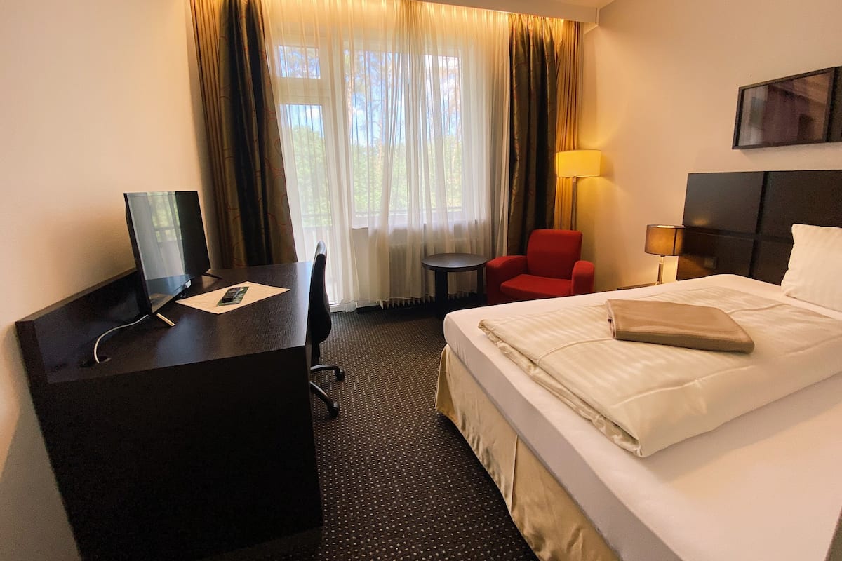 A hotel room with a bed, desk, chair, lamp, and a TV.