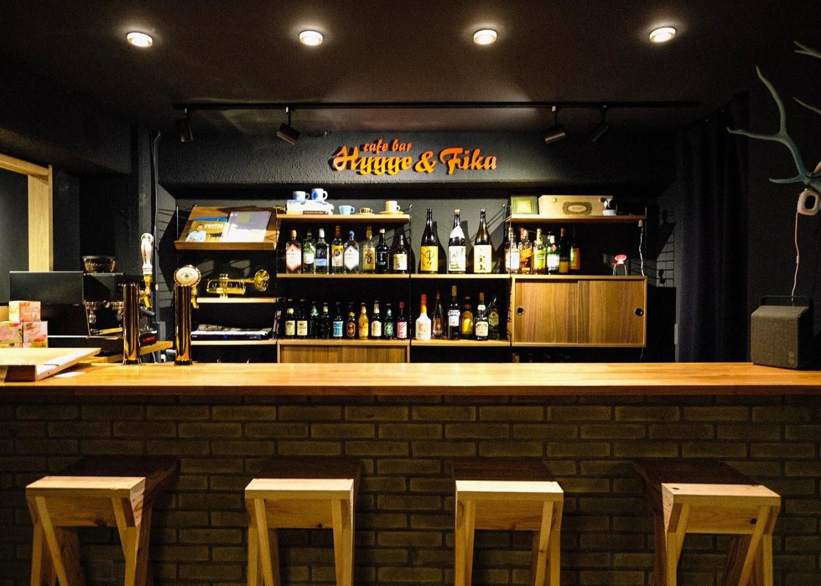 A bar with a sign reading 'cafe bar & Fika,' wooden stools, and shelves stocked with bottles.