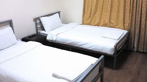 A hotel room with two single beds, a nightstand, a remote control, and a curtain. - Metropol Inn (Hounslow)