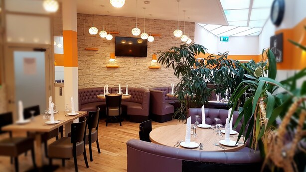 A modern restaurant with a stone wall, wooden tables, and purple seating. - Metropol Inn (Hounslow)