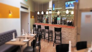 A modern restaurant with wooden flooring, black chairs, and hanging pendant lights. - Metropol Inn (Hounslow)