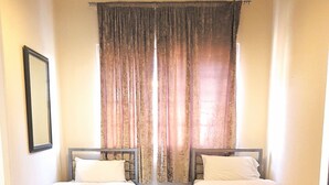 A room with two beds, a small table, and a mirror on the wall. - Metropol Inn (Hounslow)
