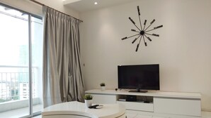 A modern living room with a flat-screen TV, a round white table, and a red sofa. - Plaza Manjalara with 2 bedrooms (Kuala Lumpur)