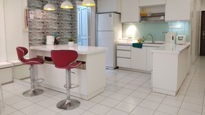 A modern kitchen with white cabinets, a central island with red bar stools, and pendant lighting. - Plaza Manjalara with 2 bedrooms (Kuala Lumpur)