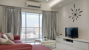 A modern living room with a red sofa, a flat-screen TV, and a large window with curtains. - Plaza Manjalara with 2 bedrooms (Kuala Lumpur)