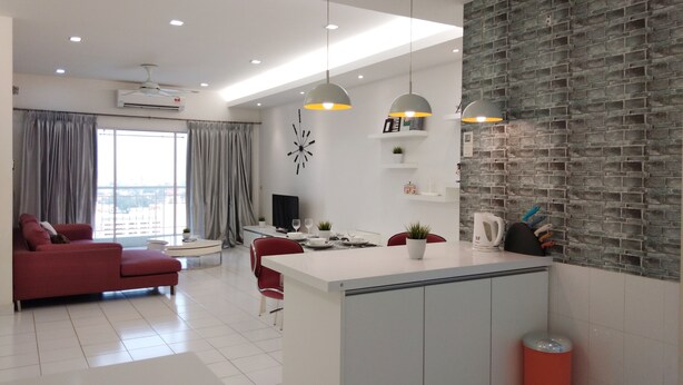 A modern apartment with a kitchen, dining area, and living room. It features a large window, a red sofa, and a kitchen island with a sink and countertop. - Plaza Manjalara with 2 bedrooms (Kuala Lumpur)