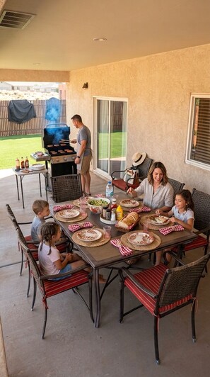 An outdoor dining area with a grill, a table set for a meal, and a view of a backyard. - Rustic home, spacious, clean, great for boaters, families, fishermen, business (Page)