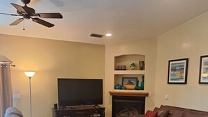 A living room with a sofa, a coffee table, a TV, a fireplace, and a ceiling fan. - Rustic home, spacious, clean, great for boaters, families, fishermen, business (Page)