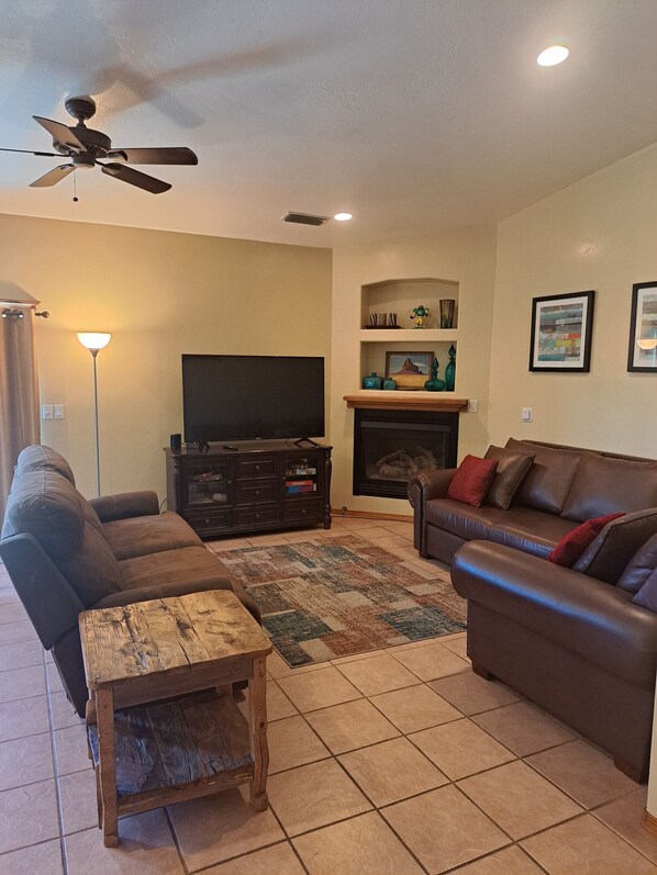 A living room with a sofa, a coffee table, a TV, a fireplace, and a ceiling fan.
