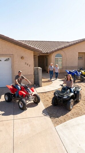 A residential driveway with two ATVs parked, a house with a garage, and a number '567' on the wall. - Rustic home, spacious, clean, great for boaters, families, fishermen, business (Page)