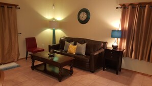 A living room with a brown leather sofa, a wooden coffee table, a red chair, a wall clock, a lamp, and a nightstand. - Rustic home, spacious, clean, great for boaters, families, fishermen, business (Page)