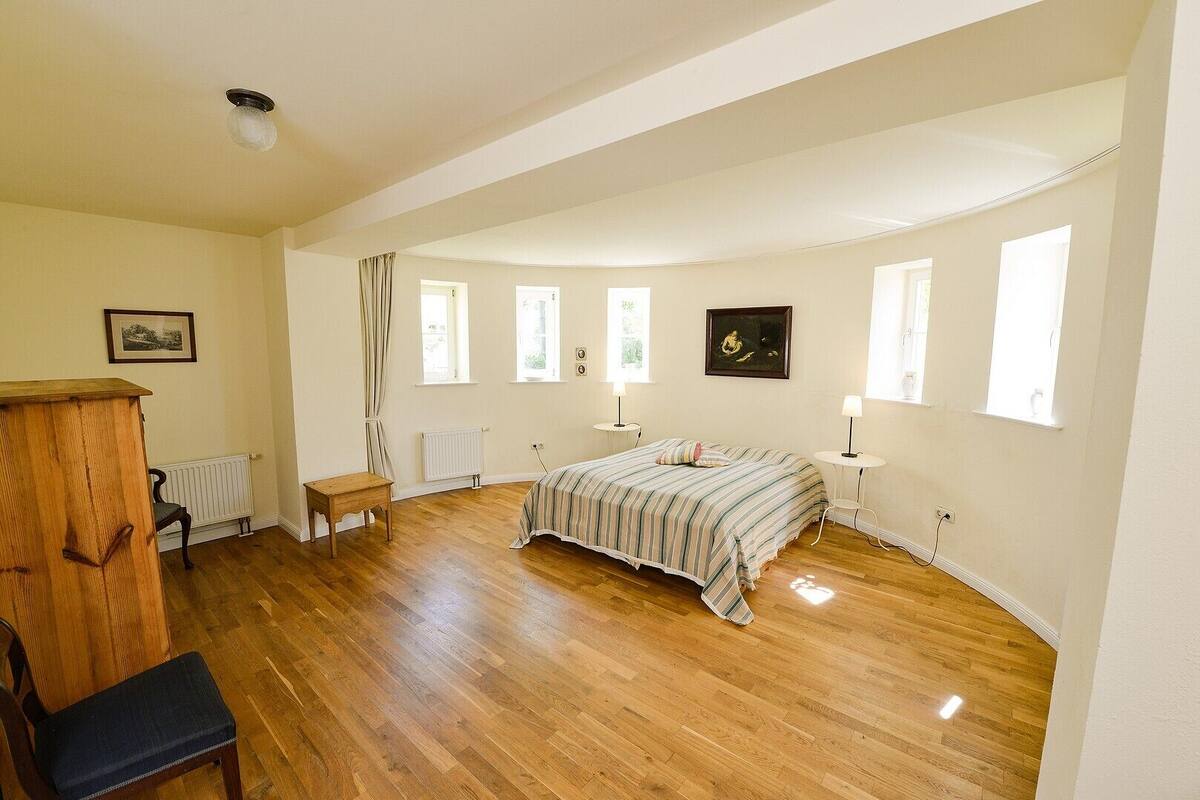 Une chambre spacieuse dotée d’un grand lit, d’un parquet et de nombreuses fenêtres qui laissent entrer la lumière naturelle.
