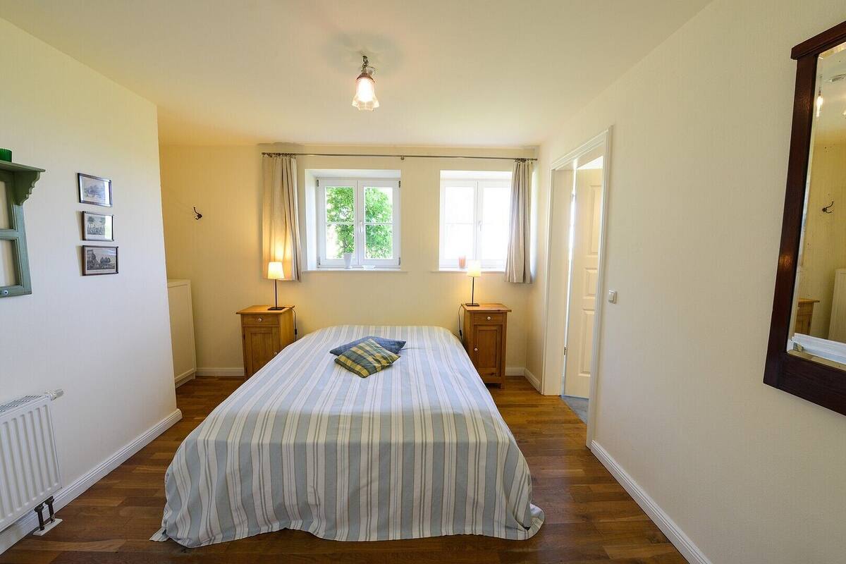 Une chambre à coucher avec un lit, deux tables de chevet, une fenêtre et un miroir.