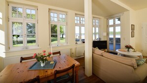 A spacious living area with a wooden dining table, a sofa, and a TV. - Gut Grubnow Rügen (Neuenkirchen)