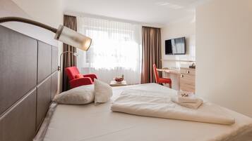Ein Hotelzimmer mit Bett, Schreibtisch, Stuhl, Fernseher und einem Fenster mit Vorhängen.