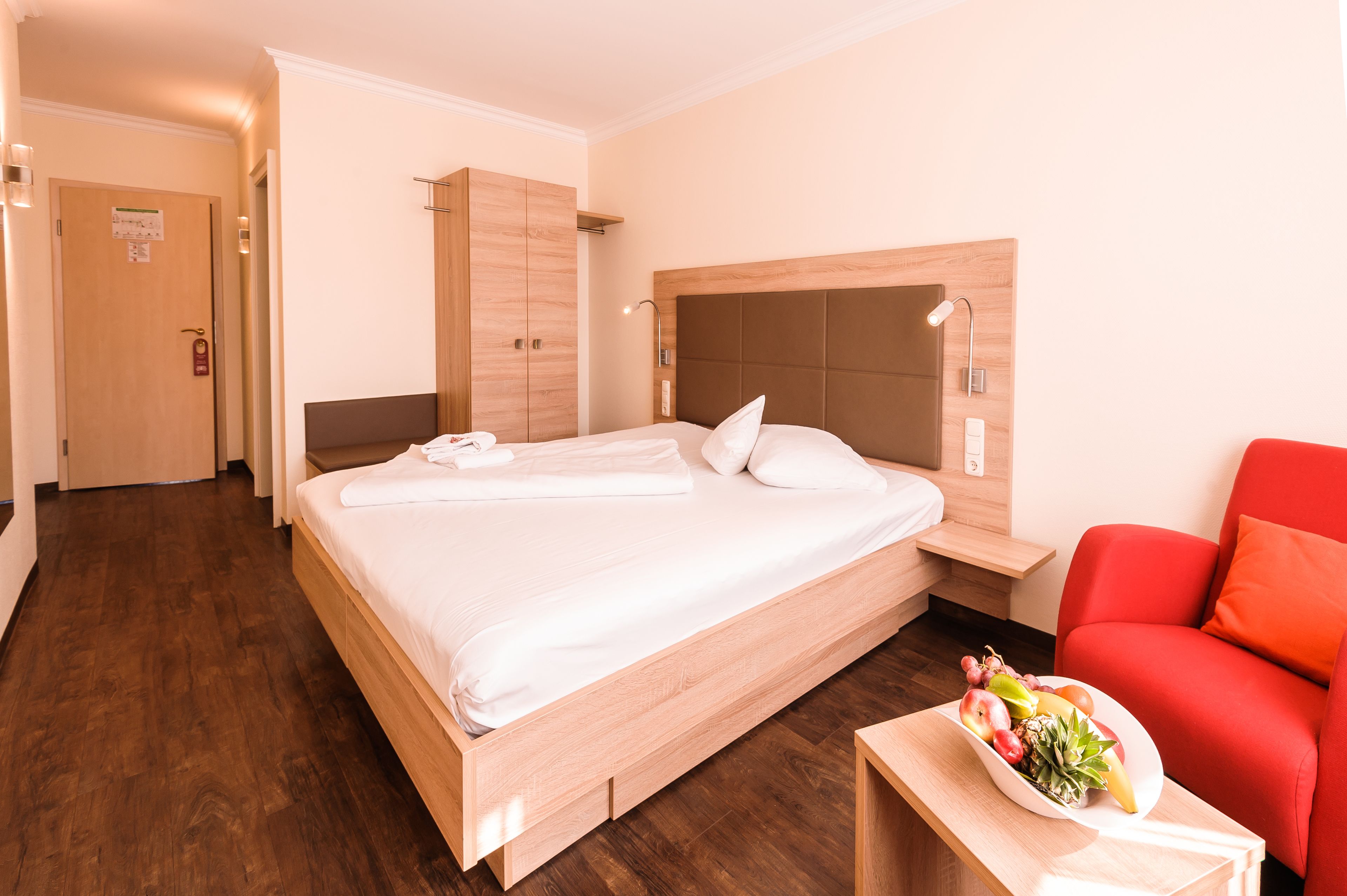 Ein Hotelzimmer mit einem großen Bett, einem Holzschrank, einem Nachttisch und einem roten Sessel.