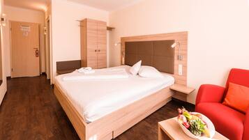 A hotel room with a large bed, wooden wardrobe, bedside table, and a red armchair.