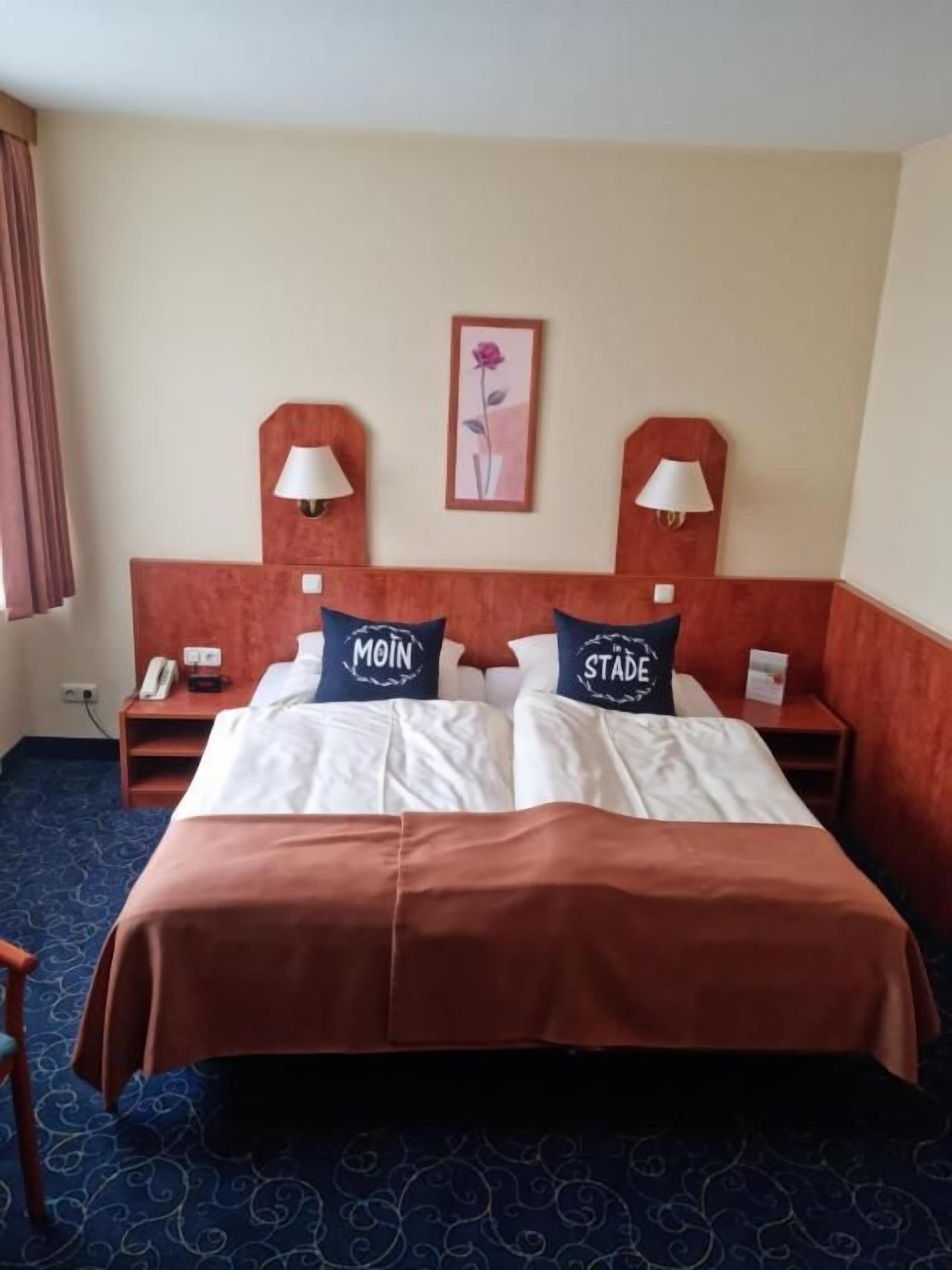 A hotel room with a large bed, two bedside tables, a nightstand, a lamp, and a framed picture on the wall.