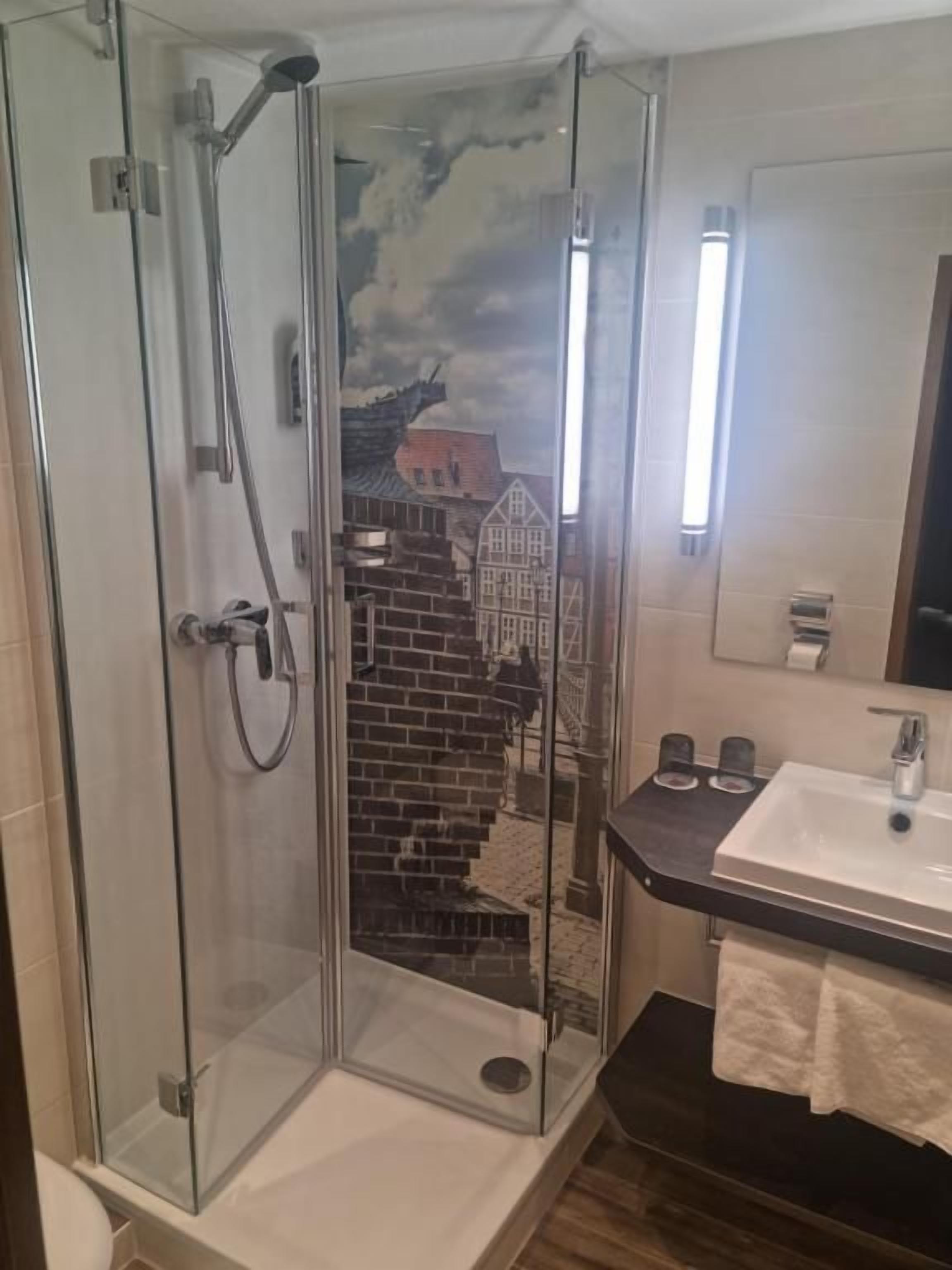 Ducha envuelta en vidrio con vista a un edificio de ladrillo, un lavamanos con espejo y un perchero para toallas.