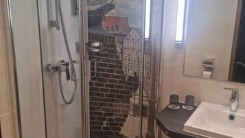 Ducha envuelta en vidrio con vista a un edificio de ladrillo, un lavamanos con espejo y un perchero para toallas.