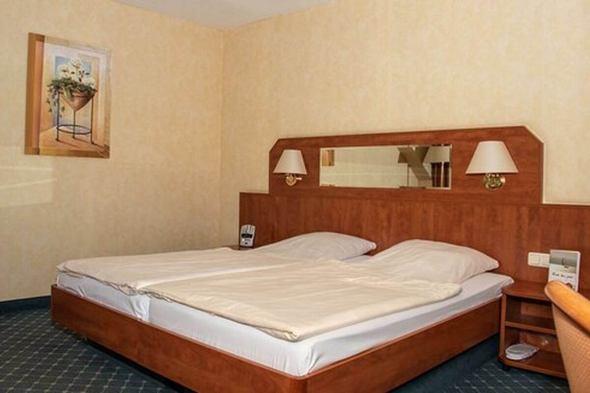 A hotel room with a wooden bed, two bedside lamps, a bedside phone, and a small table with a lamp.