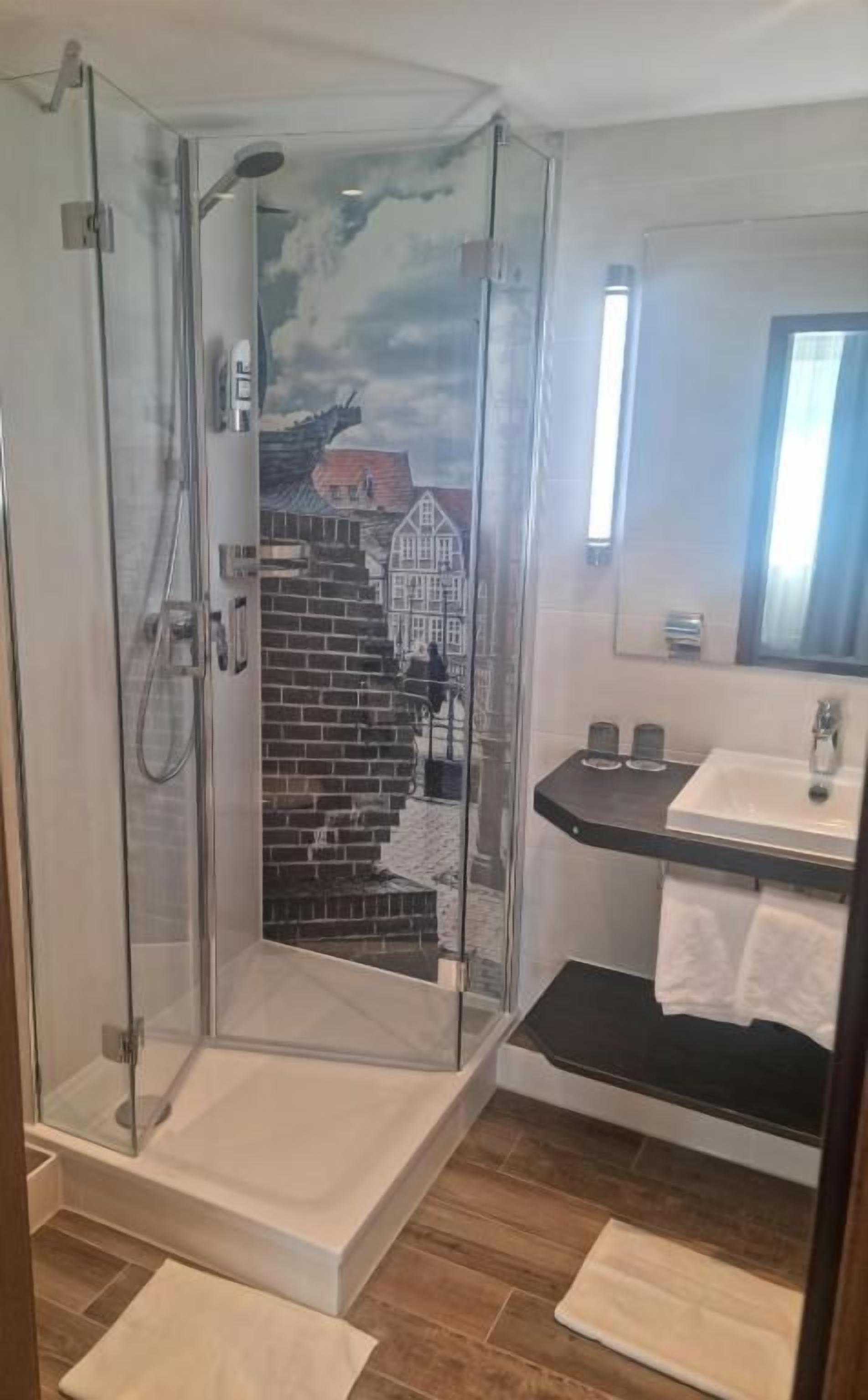 A shower with a glass door, a sink with a mirror above it, and a towel rack.