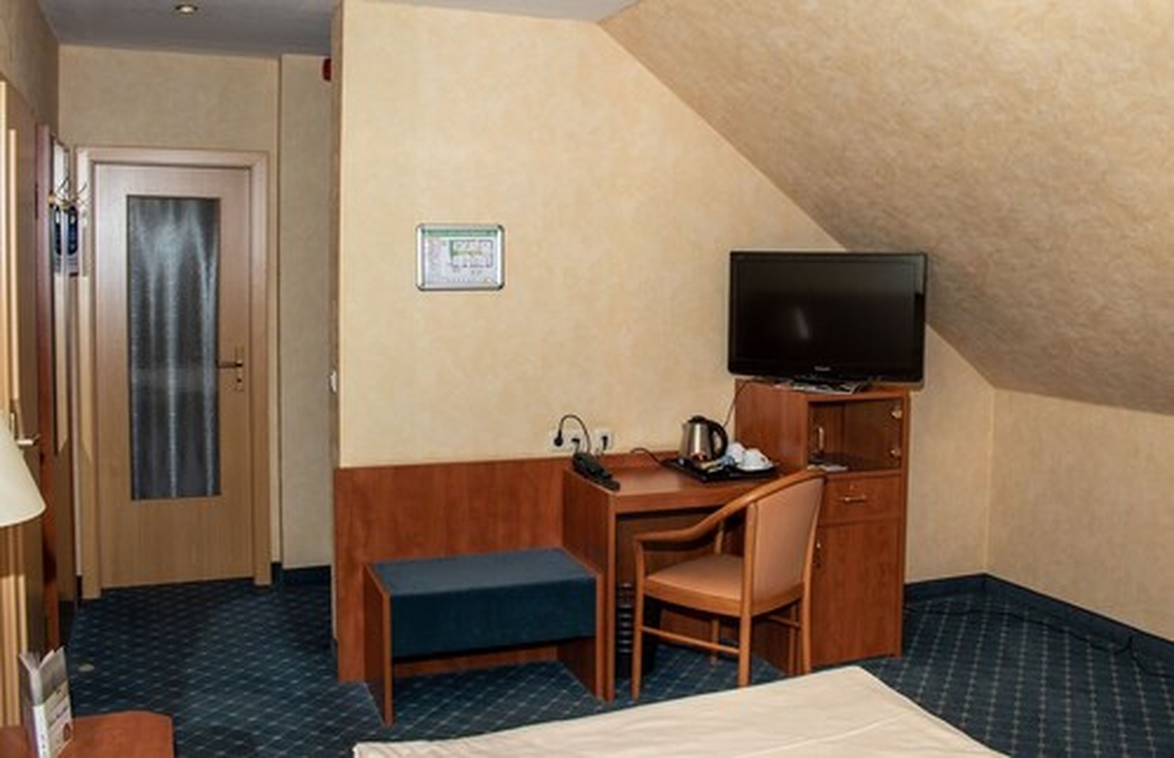 A hotel room with a bed, a desk, a chair, a television, and a small cabinet.