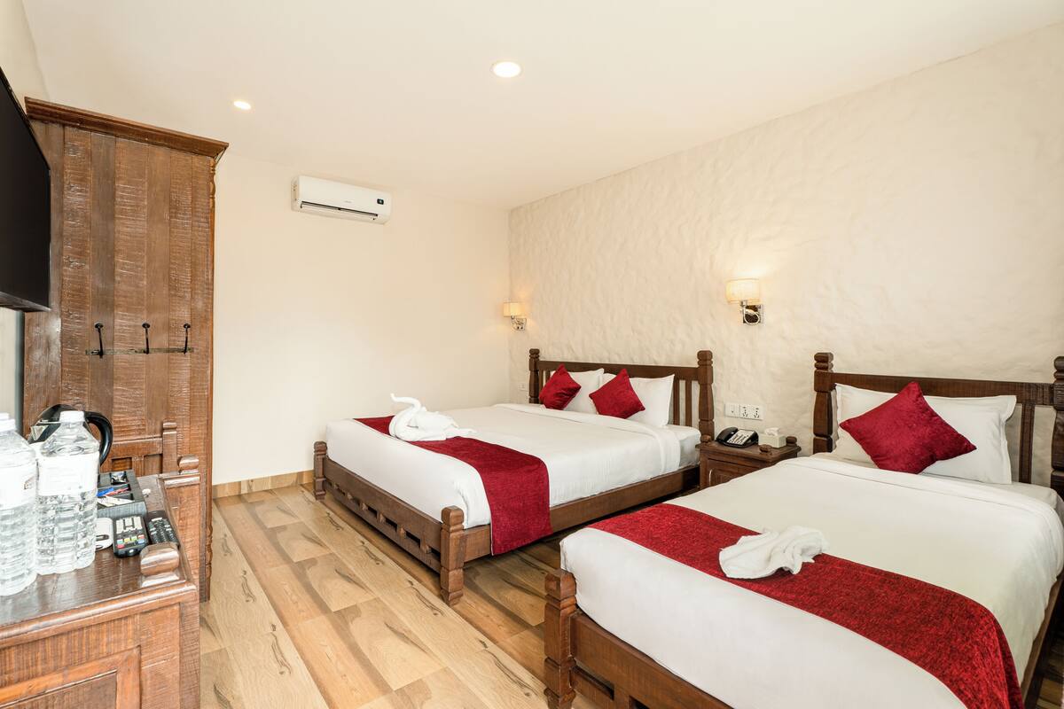 A hotel room with two beds, wooden headboards, white bedding, red throw pillows, a wooden desk with a telephone, and a minibar.