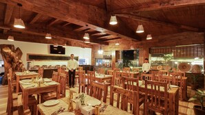 A restaurant with wooden tables and chairs, a large wooden tree trunk decoration, and a television mounted on the wall. - The Culture Resort (Pokhara)