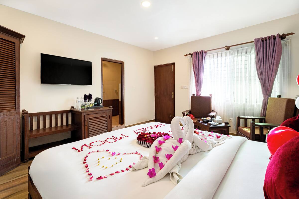 A hotel room with a bed, a flat-screen TV, a desk with a chair, and a window with curtains.