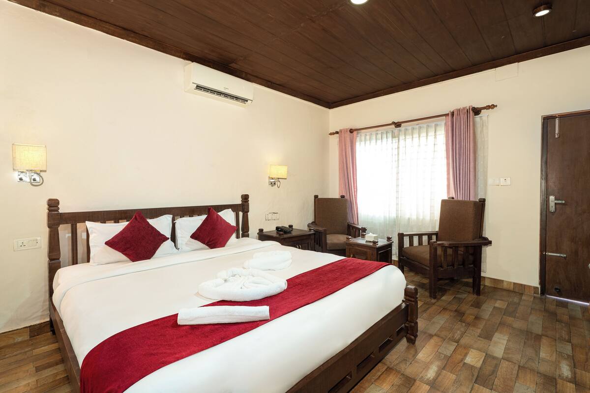 A hotel room with a wooden bed, a desk, a chair, a wardrobe, and a window with curtains.