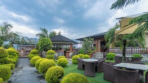 An outdoor patio area with neatly trimmed bushes, wicker furniture, and a gazebo. - The Culture Resort (Pokhara)