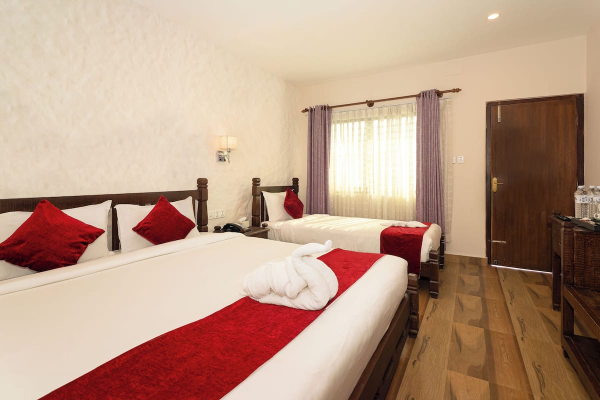 A hotel room with two beds, a wooden wardrobe, a nightstand, and a wall-mounted lamp.