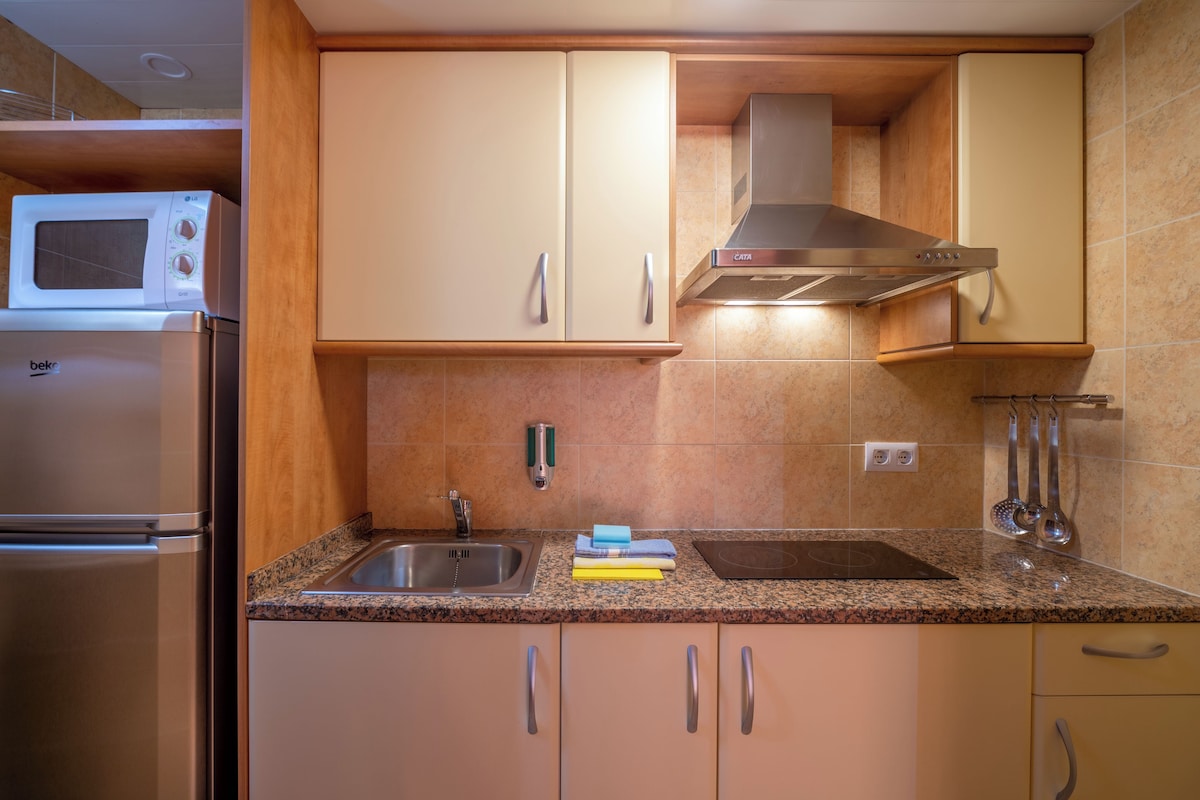 Een keuken met beige kastjes, een roestvrijstalen koelkast, een magnetron, een spoelbak en een afzuigkap.