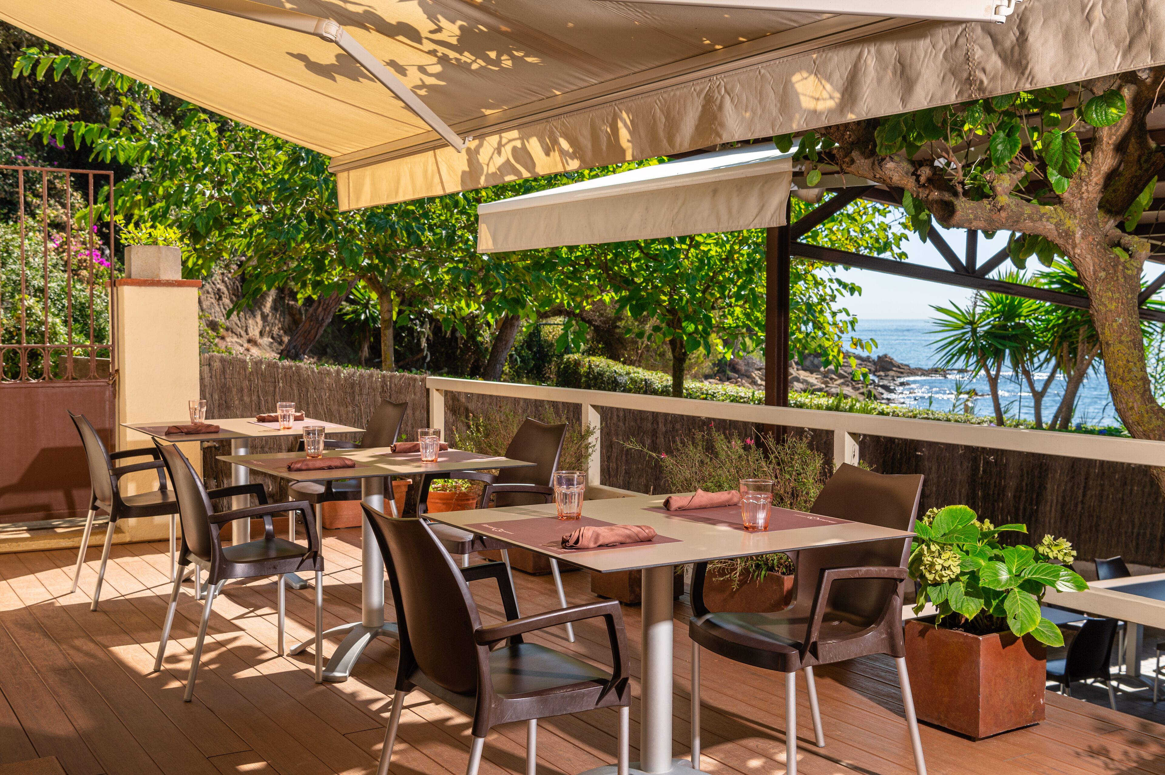 An outdoor dining area with tables and chairs, surrounded by greenery and overlooking a scenic view.